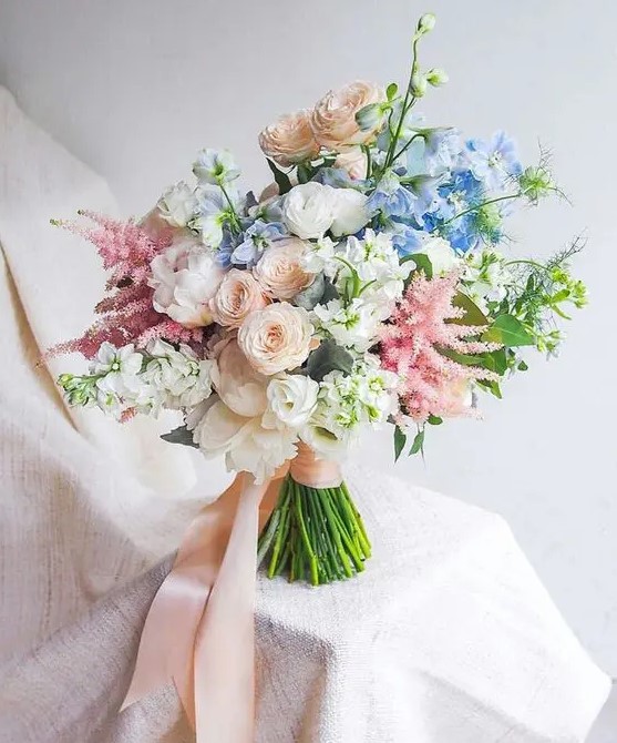 a dreamy wedding bouquet of white peonies, blush and white ranunculus, astilbe, blue blooms and blush ribbons for a garden bride