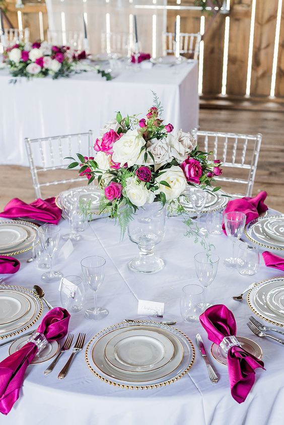 a contrasting wedding tablescape in neutrals and with magenta napkins plus a white and magenta flower centerpiece is amazing