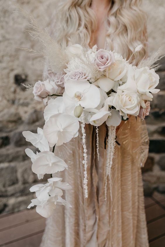 a jaw-dropping cascading wedding bouquet of white orchids, white and pale pink roses, pampas grass and some twigs