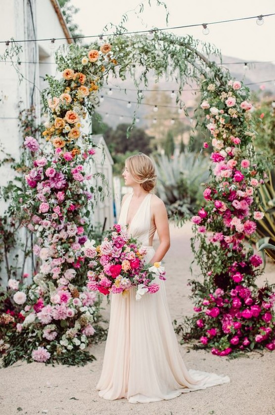 a lovely ombre floral wedding arch with blush, orange, pink, white and hot pink blooms and greenery is wow
