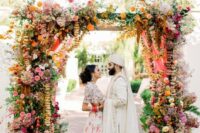 24 a colorful wedding arch with much greenery, bright florals and hanging ribbons and blooming branches for a bold wedding