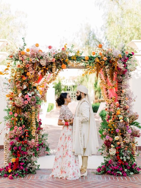 a colorful wedding arch with much greenery, bright florals and hanging ribbons and blooming branches for a bold wedding