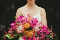24 a dimensional and textural cascading wedding bouquet of fuchsia blooms, pincushion proteas, king proteas, greenery and leaves for a bold wedding
