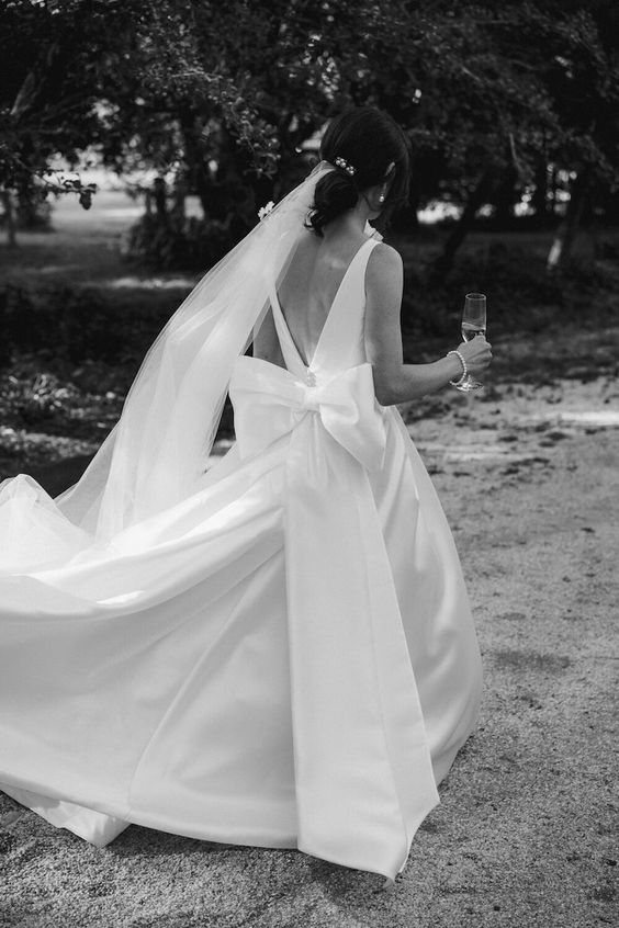a refined wedding ballgown with a cutout back, a large bow, a long train plus a veil are a fantastic combo for a modern wedding