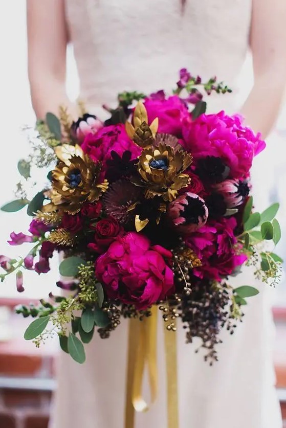 a dramatic bridal bouquet of fuchsia peonies, deep purple blooms, gold faux flowers, greenery and gilded seeded eucalyptus
