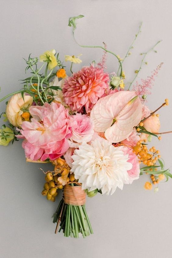 a pastel wedding bouquet with pink ranunculus, dahlias, yellow blooms, berries and greenery for a spring or summer bride