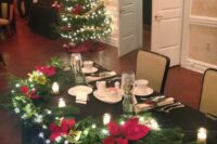 27 a sweetheart wedding tablescape with a black tablecloth, candles, an evergreen garland with lights and red poinsettias