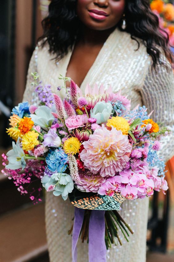 a vibrant wedding bouquet that includes pink, blue, yellow and hot pink blooms and a bold wrap plus ribbons