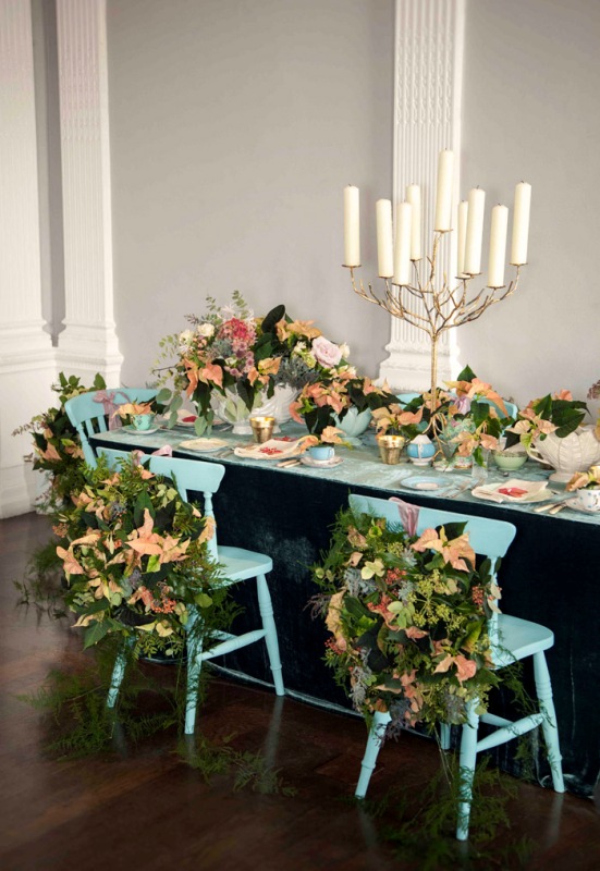 leafy chair decorations scattered with loose fern-like sprigs and peach-colored poinsettias offer an air of botanical garden magic