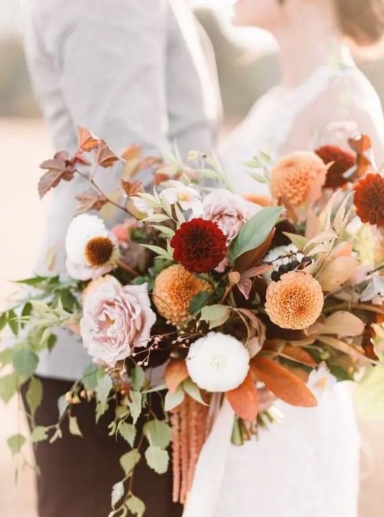 a beautiful fall wedding bouquet of white, pink, burgundy, orange blooms, greenery and dark foliage with much dimension is amazing
