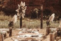 33 a boho Western wedding ceremony space with an arch decorated with pampas grass and greenery, cowhide rugs on the aisle