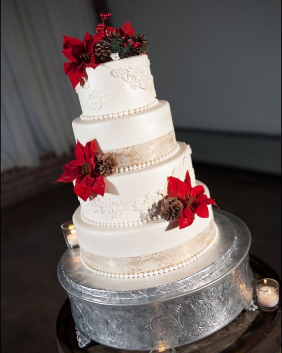 a classic winter wedding cake in white, with sugar patterns, beads, red poinsettias, pinecones, berries and evergreens