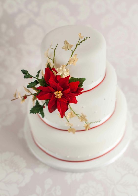 a white wedding cake with red ribbon, a faux poinsettia, greenery and berries is a classic idea for a winter wedding