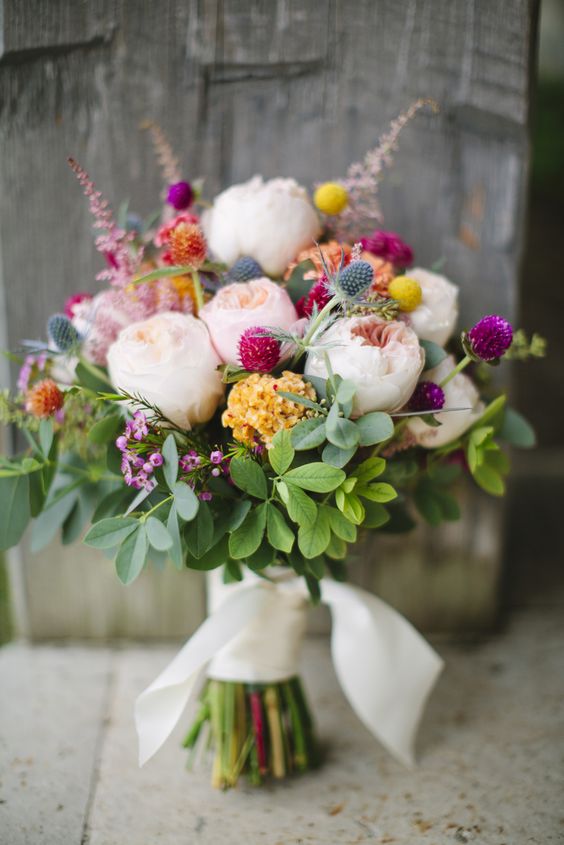 a cheerful summer wedding bouquet of blush peony roses, yellow blooms, thistles, bold and colorful flower touches and greenery