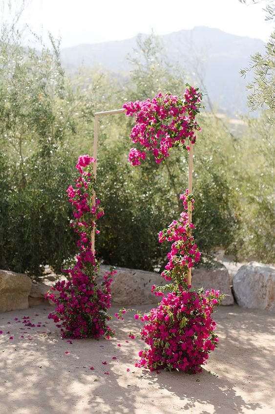 a stylish modern wedding arch decorated with magenta blooms and greenery is a cool idea for a summer or fall wedding