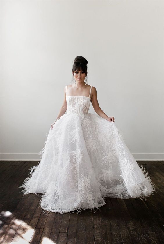 a modern wedding ballgown with spaghetti straps and a full skirt with a train and feathers on it
