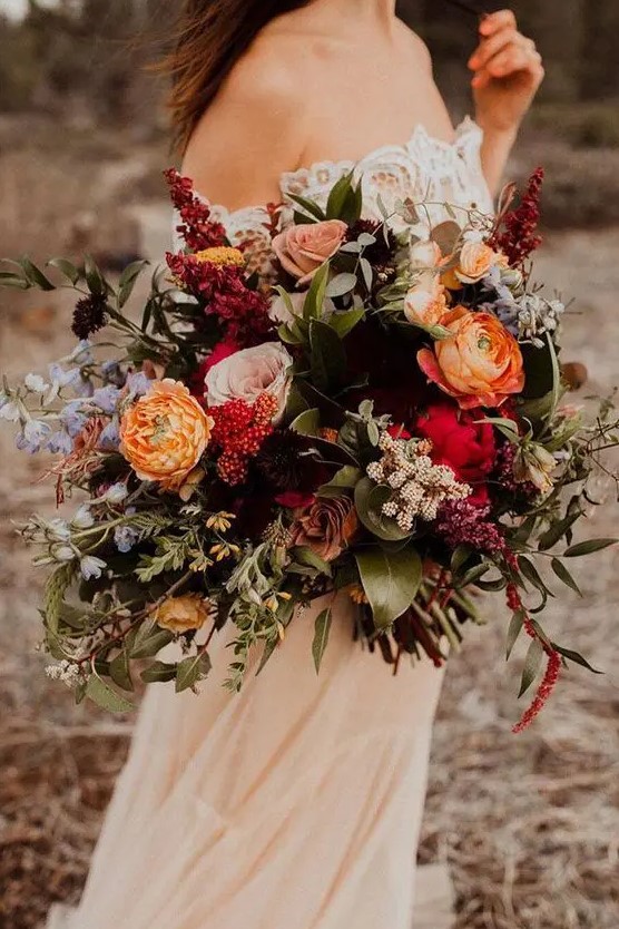 a colorful fall wedding bouquet of orange, pink, red, blue, lilac blooms, foliage and greenery is a catchy fall wedding solution