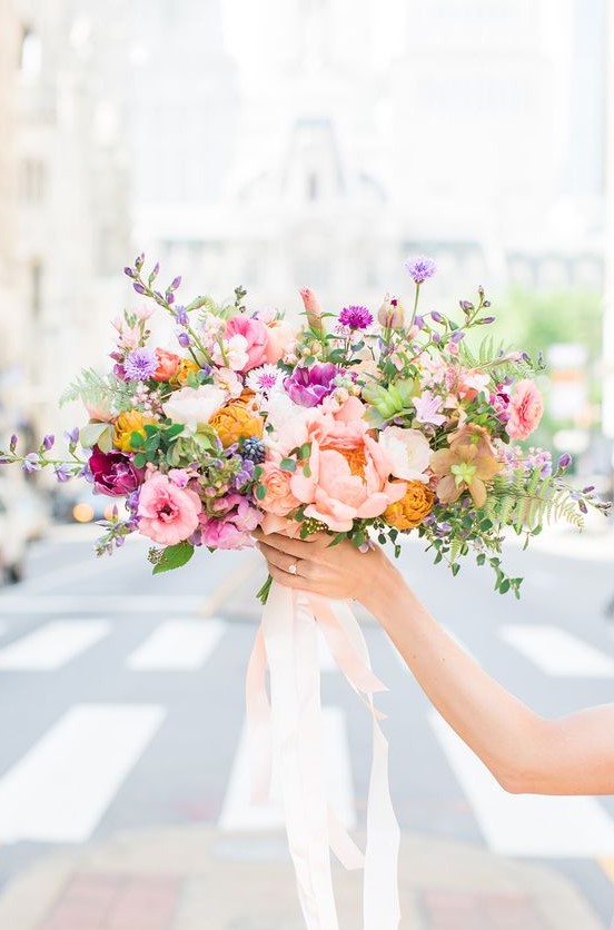 a colorful spring wedding bouquet with hot pink, blush, mustard and lilac blooms with blush ribbons