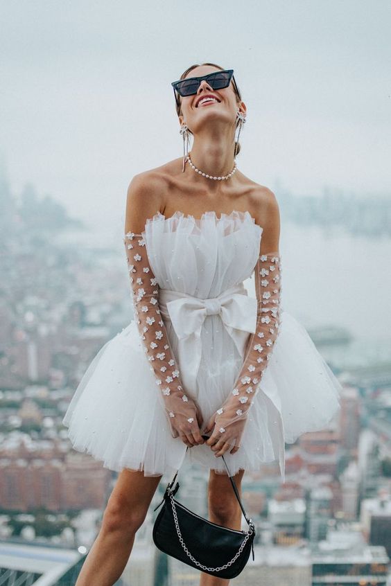 a bold bridal look with a trapless A-line mini dress with a bow, sheer floral long gloves and a pearl necklace