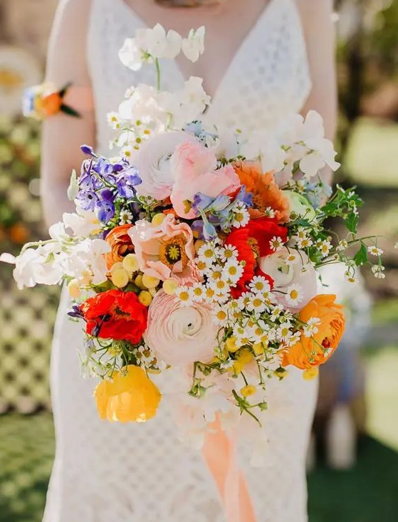 a colorful wedding bouquet with pink and yellow ranunculus, white and blush blooms, bold red touches and greenery