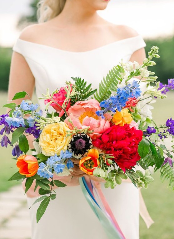 a colorful wedding bouquet with red, blush, yellow, orange, blue and purple blooms, greenery and fern for summer