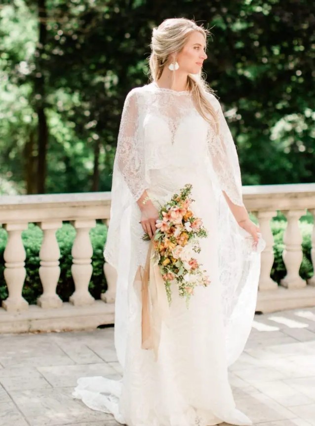 a lace A-line wedding dress paired with a matching lace capelet and delicate earrings for a strong Old World feel