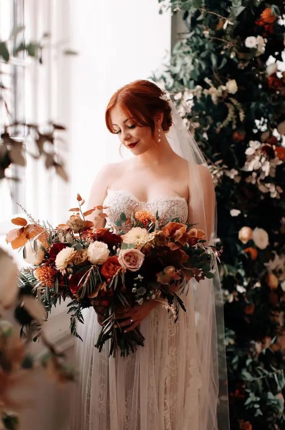 a fantastic lush and dimensional wedding bouquet of pink, blush, burgundy, rust blooms, greenery and berries plus bold fall leaves is gorgeous