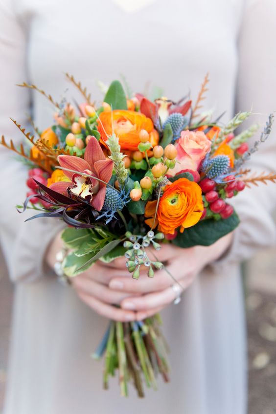 a bright and cool fall wedding bouquet with orange ranunculus, roses, orchids, berries, thistles and greenery
