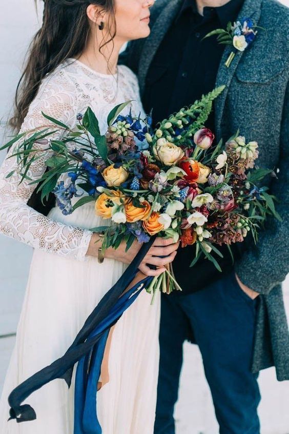 a bright wedding bouquet of bold blue, yellow, burgundy and neutral blooms, greenery and berries plus ribbons