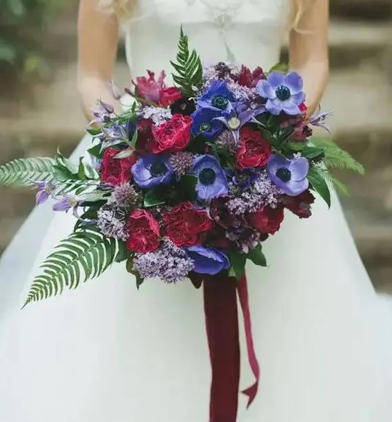 a fantastic and bold fall wedding bouquet with purple anemones, burgundy roses and lilac blooms, greenery and foliage