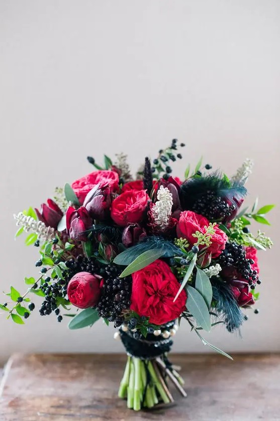 a sumptuous fall wedding bouquet of deep purple, pink and red blooms, lots of privet berries and greenery plus feathers for a fall bride