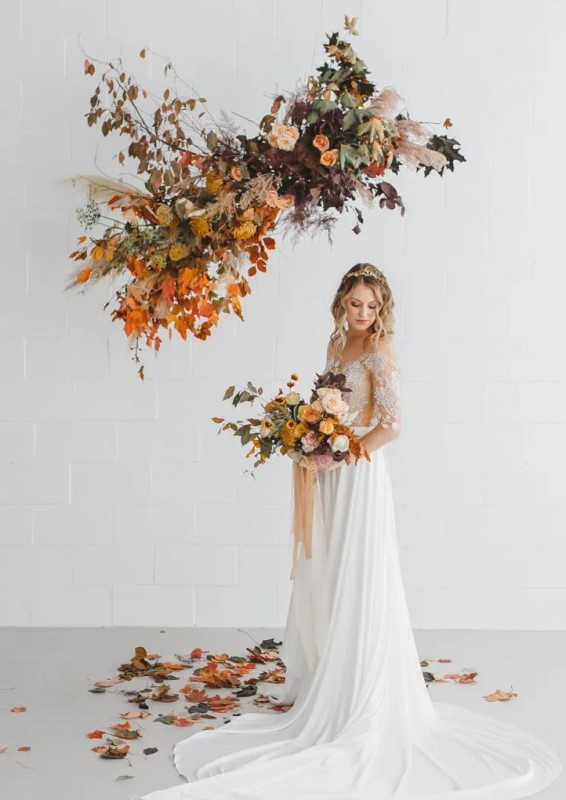 a beautiful and chic floral on air wedding altar with orange and yellow blooms, greenery, dark foliage and twigs, pampas grass