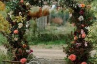 a beautiful garden wedding arch covered with leaves, blush, white, deep and bright red blooms is a very chic and bold idea for fall