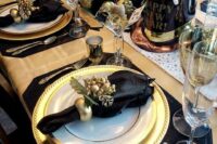a black and gold wedding tablescape with black placemats, napkins, a top hat and a whimsical centerpiece in black and gold
