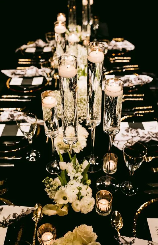 a black and white NYE wedding tablescape with black and white menus, white blooms, floating candles and gold cutlery