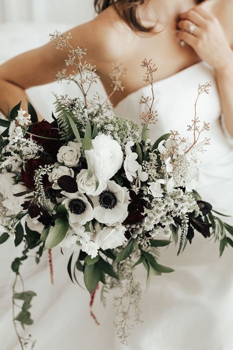 a black and white textural wedding bouquet of white roses and ranunculus, dark blooms and white anemones plus greenery and twigs