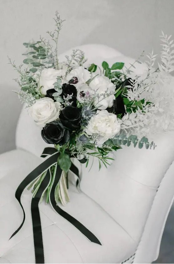 a black and white wedding bouquet of roses, greenery, thistles and white leaves plus black ribbons is amazing