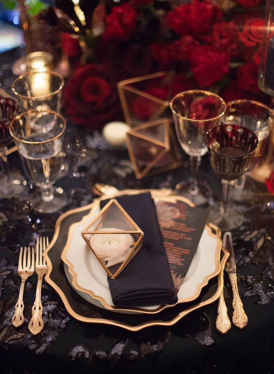 a bright NYE wedding tablescape with a black sequin tablecloth, red roses, gold-rimmed glasses and plates is amazing