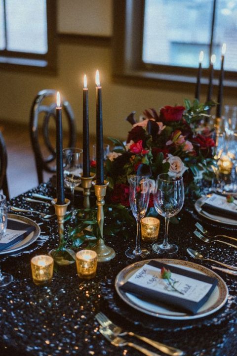 a bright and bold NYE wedding table with a black sequin tablecloth, black and tealight candles, bright blooms and black napkins