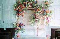 a bright floral wedding backdrop of greenery and colorful floral arrangements and matching floral arrangements to line up the aisle