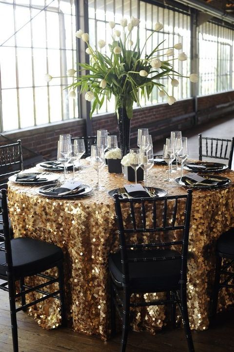 a bright wedding tablescape with a gold sequin tablecloth, black plates, white blooms in a black vase