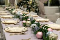 a chic NYE or Christmas table setting with neutral gold-rimmed plates, gold, silver and pink ornaments, greenery and tall and thin candles