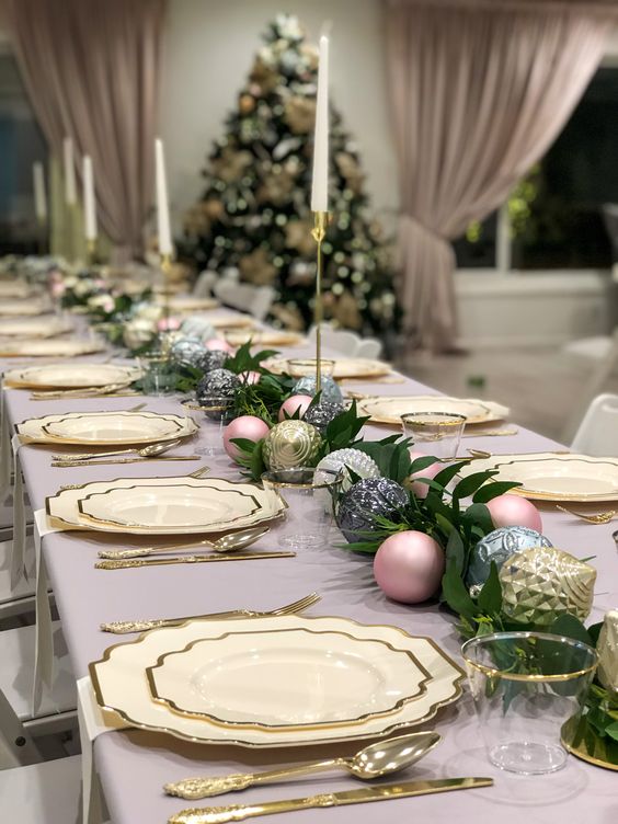 a chic NYE or Christmas table setting with neutral gold rimmed plates, gold, silver and pink ornaments, greenery and tall and thin candles