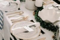 a chic and bright NYE wedding tablescape with a greenery runner, white candles, shiny ornaments and striped napkins