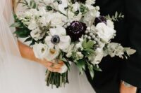 a chic wedding bouquet of white ranunculus, anemones, dark dahlias, greenery and berries is amazing