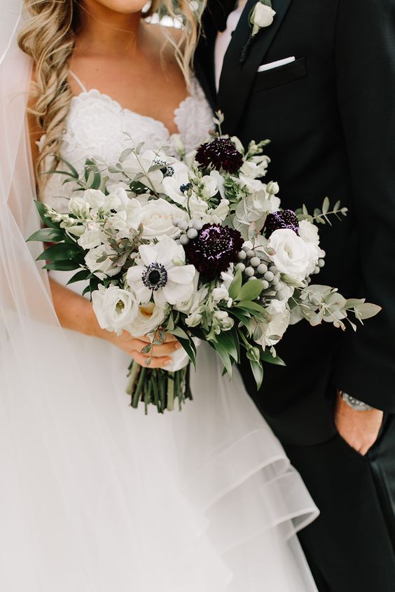 a chic wedding bouquet of white ranunculus, anemones, dark dahlias, greenery and berries is amazing
