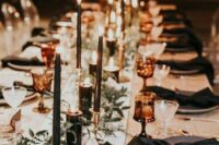 a chic wedding reception table with black candles, plates and napkins, greenery and copper touches