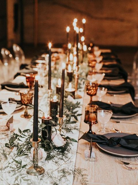a chic wedding reception table with black candles, plates and napkins, greenery and copper touches