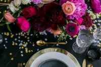 a colorful NYE wedding tablescape with a black tablecloth and a plate, a gold charger and cutlery, a bold floral centerpiece and confetti
