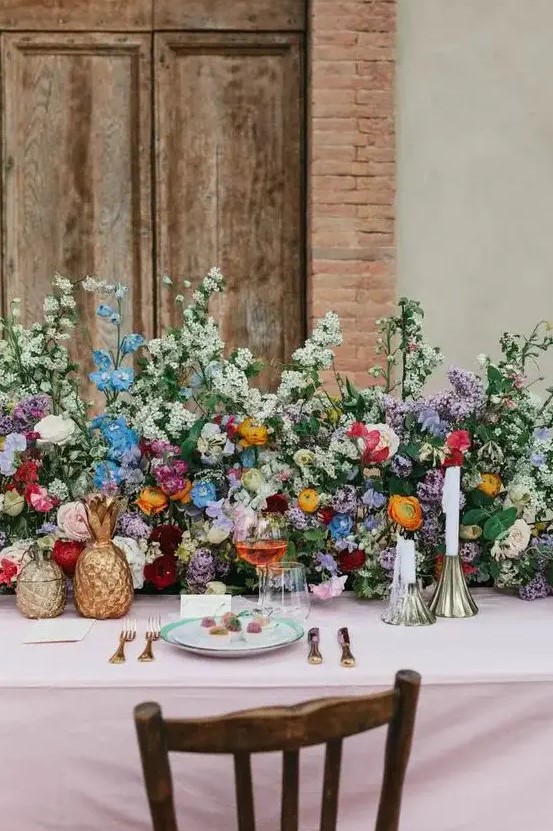 a colorful garden wedding table setting with a super lush greenery and bold floral table runner, brass candleholders and gold pineapples